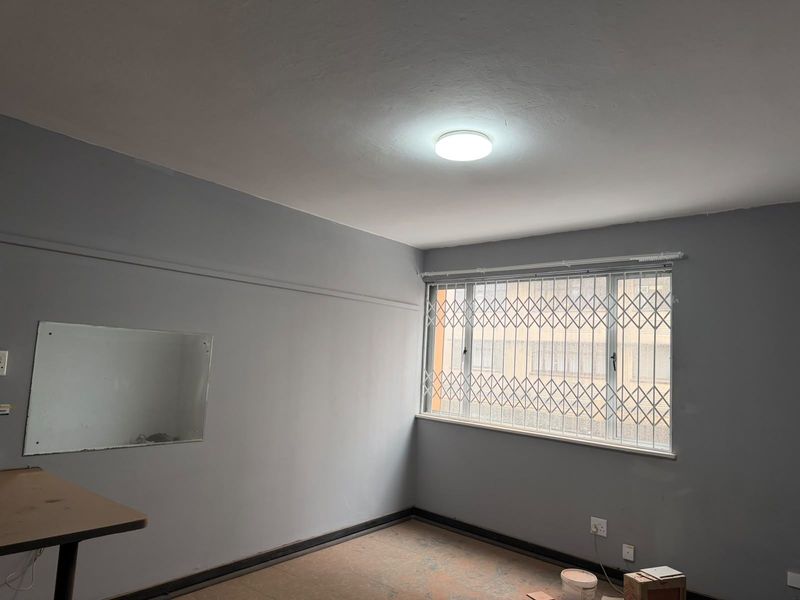 An empty bedroom featuring grey walls, a window with a security gate, and basic electrical fixtures, ready for renovation or staging.