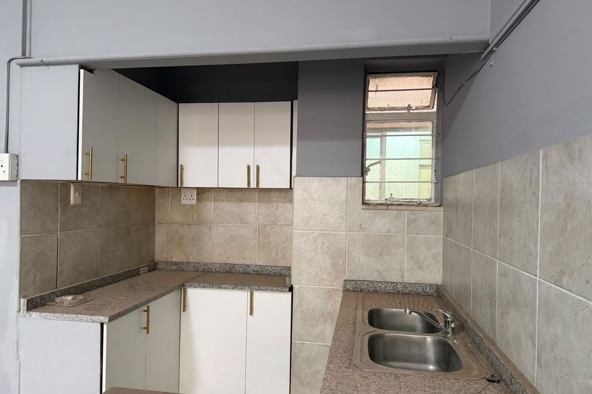 A compact kitchen featuring white built-in cabinetry, granite countertops, a double basin sink, and tiled backsplash, offering a functional layout for renovation.