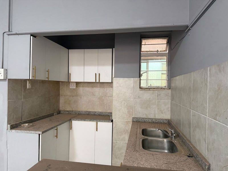 A compact kitchen featuring white built-in cabinetry, granite countertops, a double basin sink, and tiled backsplash, offering a functional layout for renovation.