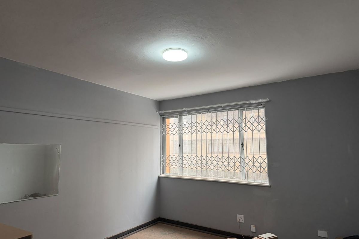 An empty bedroom featuring grey walls, a window with a security gate, and unfinished flooring, ready for final finishes and personal touches.