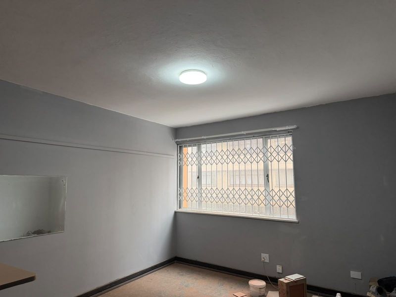 An empty bedroom featuring grey walls, a window with a security gate, and unfinished flooring, ready for final finishes and personal touches.