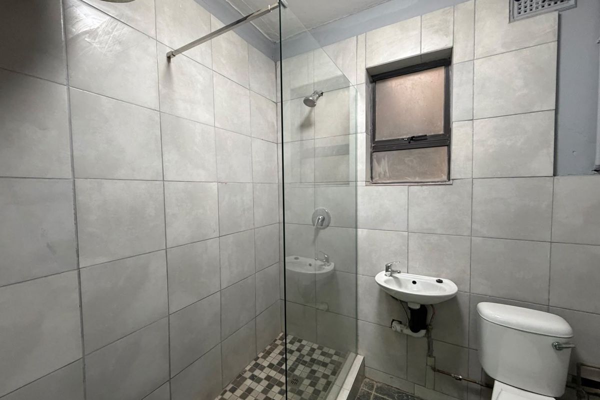 A compact bathroom featuring a glass-enclosed shower, wall-mounted basin, and toilet with neutral wall tiling and dark floor tiles.