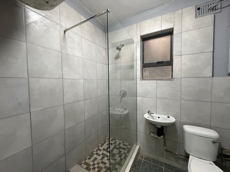 A compact bathroom featuring a glass-enclosed shower, wall-mounted basin, and toilet with neutral wall tiling and dark floor tiles.