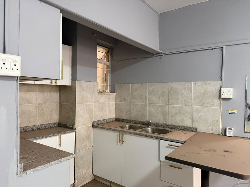 A functional kitchen featuring built-in cabinetry, laminate countertops, a double bowl stainless steel sink, and tiled backsplash.