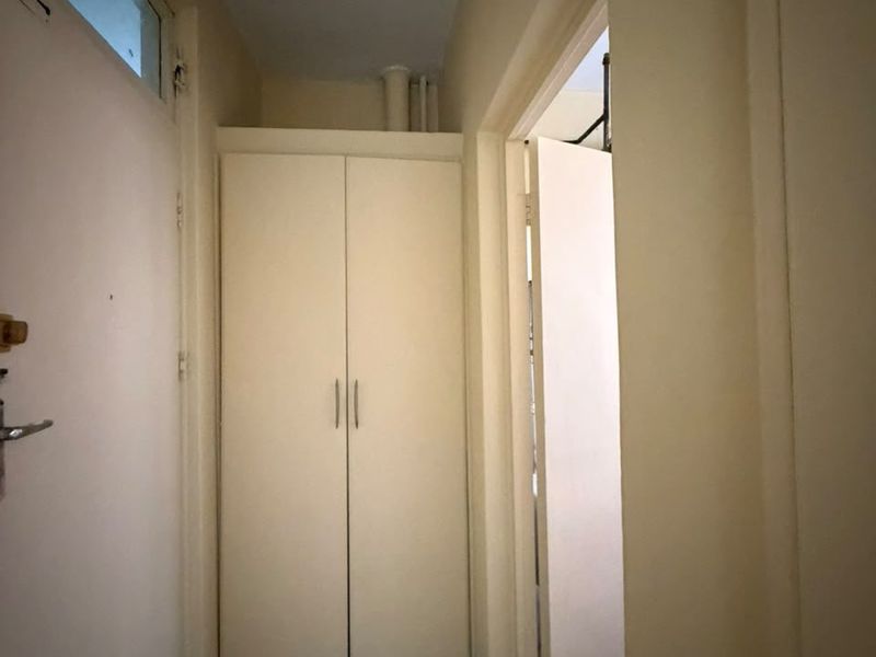 A functional hallway featuring a built-in storage cupboard and a transom window above the door frame.