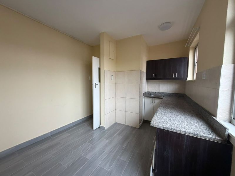 A functional, empty kitchen featuring granite countertops, dark wood cabinetry, tiled backsplash, and modern grey floor tiles.