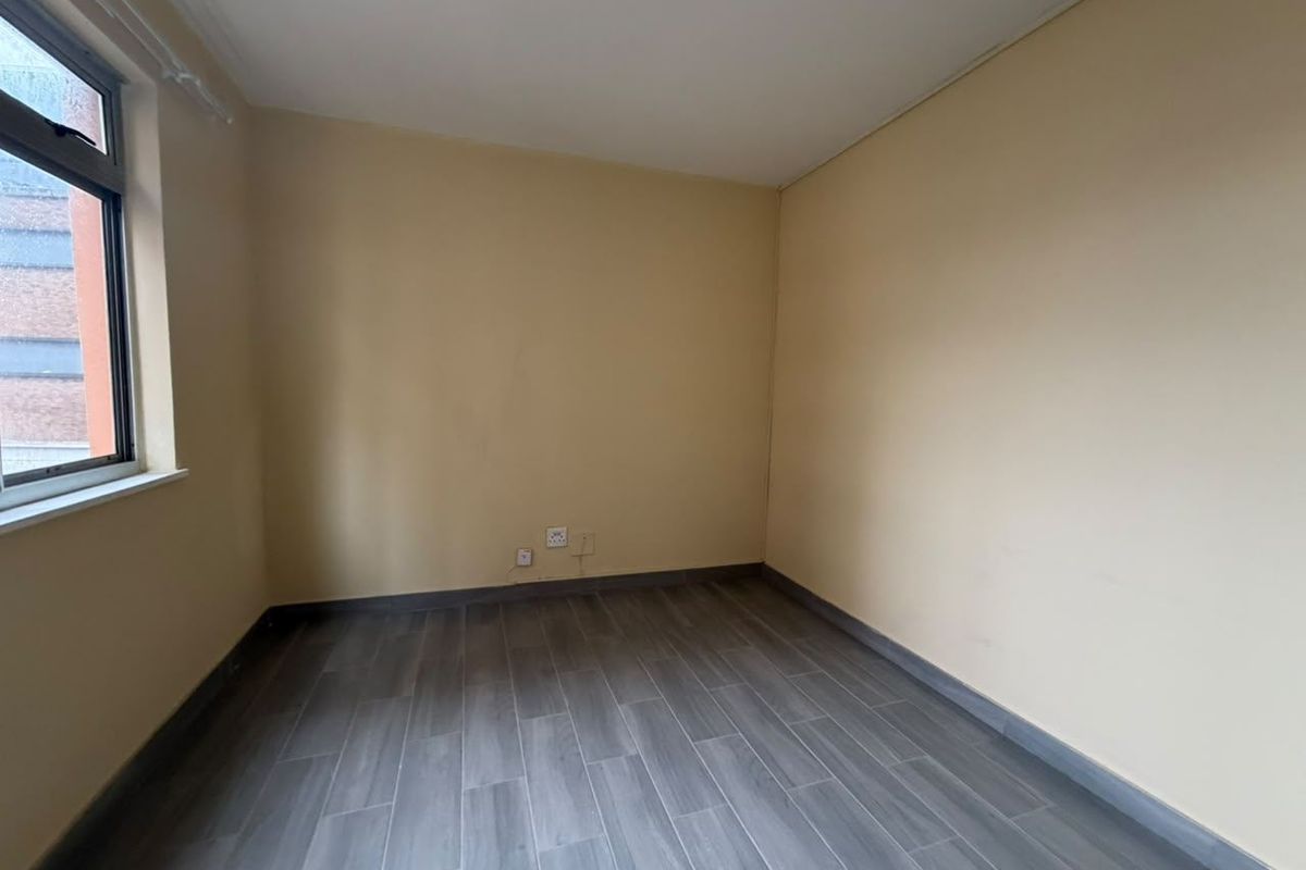An empty bedroom featuring grey wood-look tile flooring, neutral walls, and a single casement window.