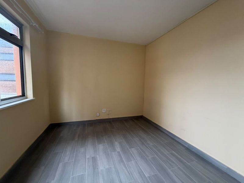 An empty bedroom featuring grey wood-look tile flooring, neutral walls, and a single casement window.