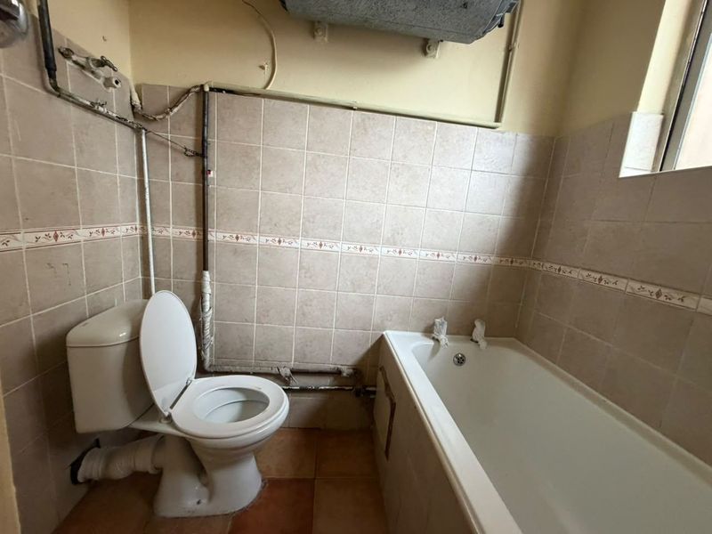 A dated bathroom featuring a standard bathtub and toilet with exposed plumbing and tiled finishes, requiring modernization and cosmetic updates.