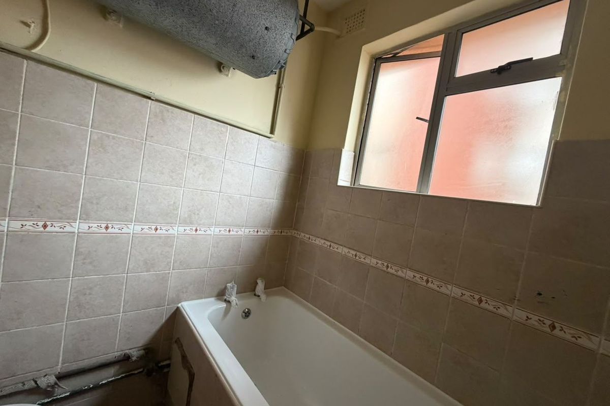 A dated bathroom featuring a standard bathtub, tiled walls, and an exposed electric water heater unit, requiring modernization and cosmetic updates.