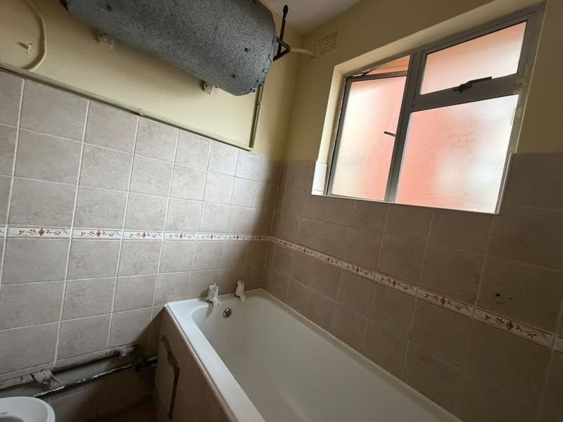 A dated bathroom featuring a standard bathtub, tiled walls, and an exposed electric water heater unit, requiring modernization and cosmetic updates.