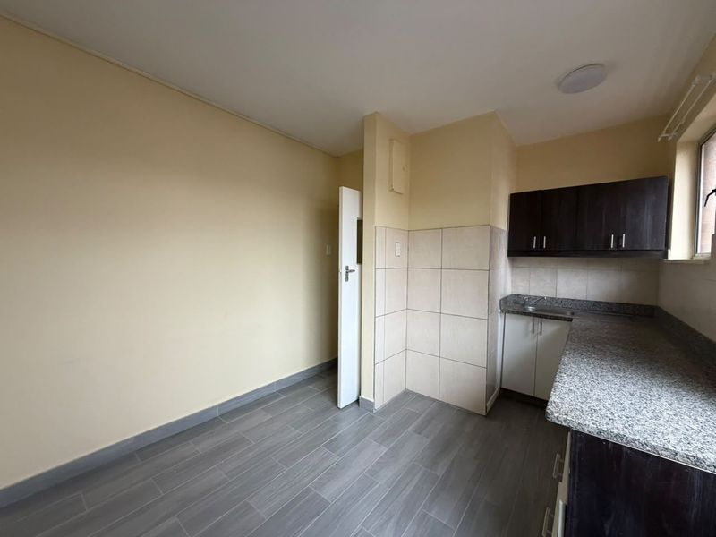 A compact, empty kitchen featuring granite countertops, dark upper cabinetry, light lower cabinets, and neutral tiled flooring and splashbacks.