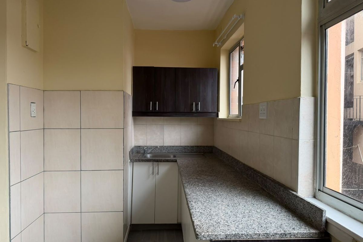 A compact kitchen featuring granite countertops, stainless steel sink, and a combination of upper and lower cabinetry with tiled splashbacks.