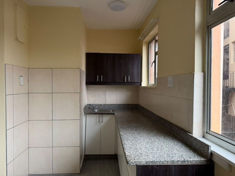 A compact kitchen featuring granite countertops, stainless steel sink, and a combination of upper and lower cabinetry with tiled splashbacks.