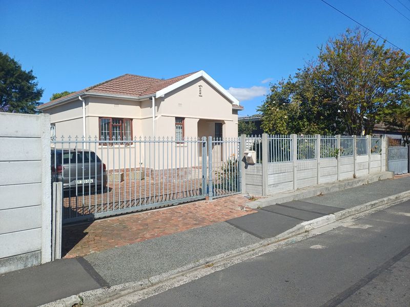 Front view of a single-story house featuring a tiled roof, brick driveway, and secure metal gate with precast concrete boundary walling.