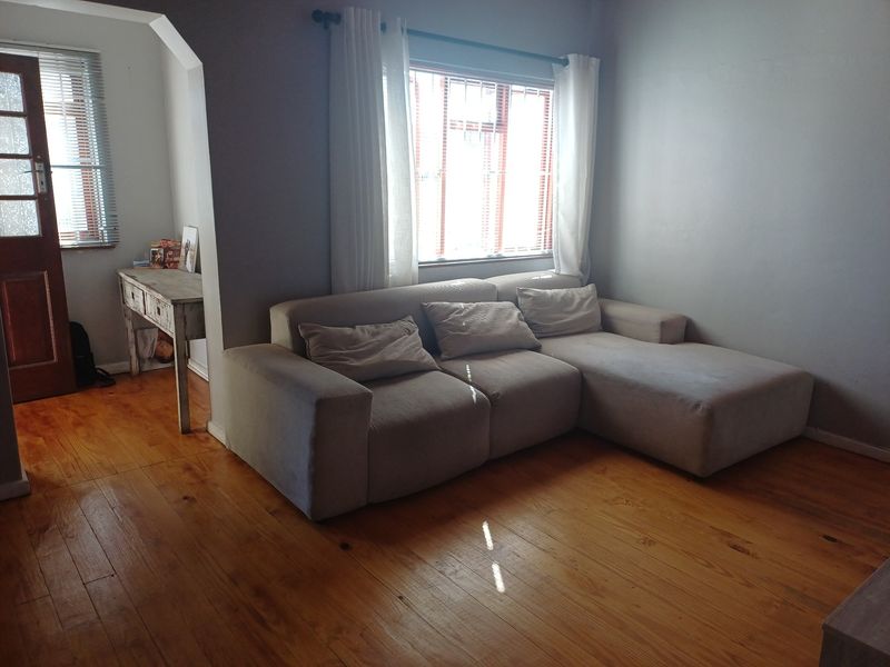 A living room featuring warm timber flooring, an arched transition to an adjacent space, and natural light through window blinds.