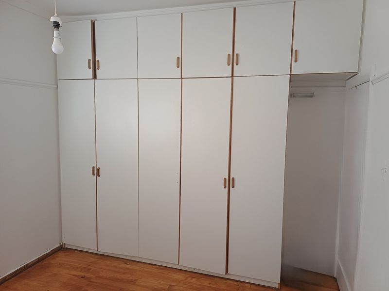 A bedroom featuring extensive white built-in cabinetry with overhead storage and polished hardwood flooring.