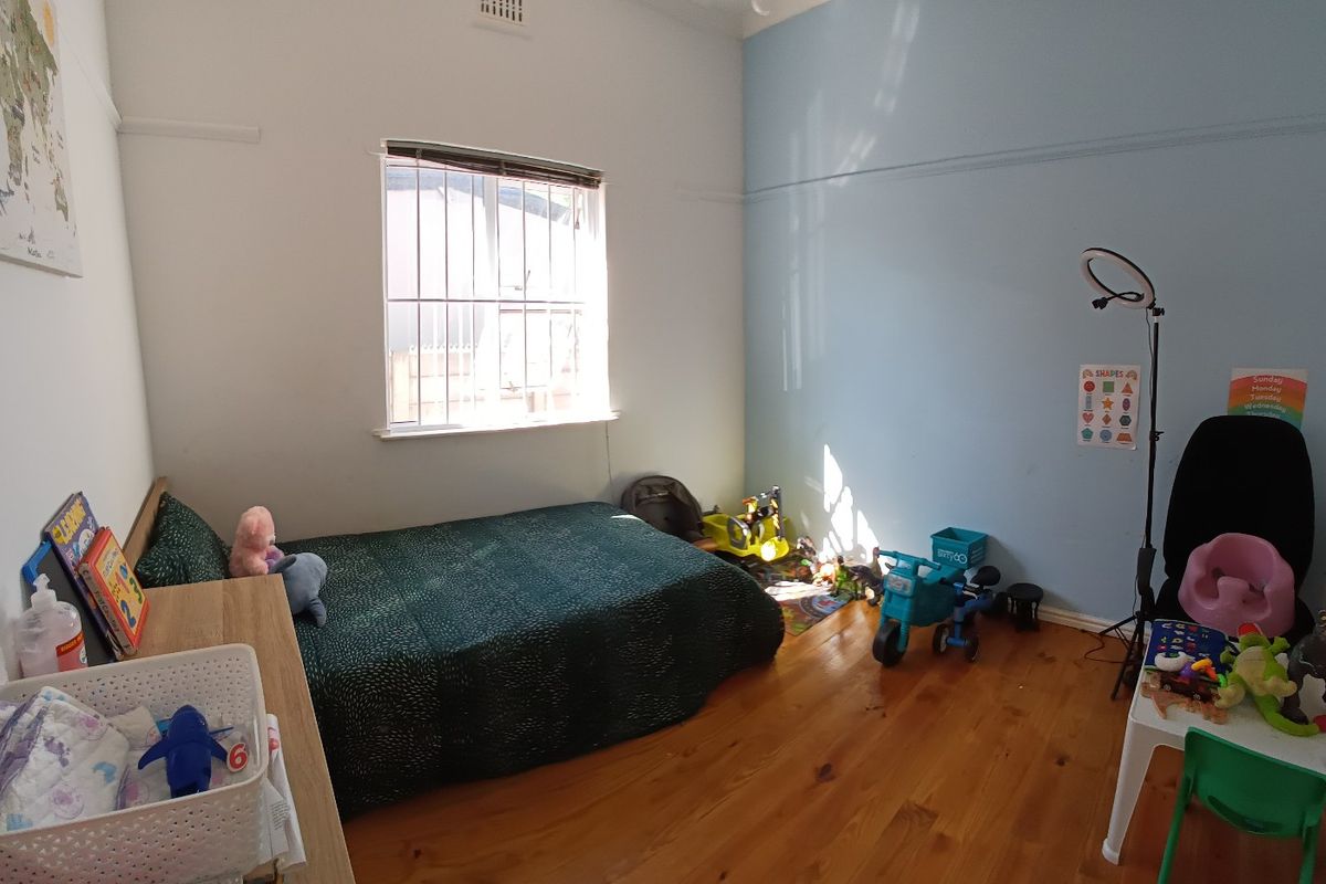 A bedroom featuring polished timber flooring, a picture rail, and a window fitted with security bars.