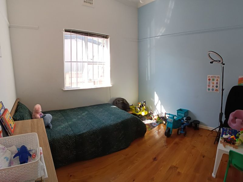 A bedroom featuring polished timber flooring, a picture rail, and a window fitted with security bars.