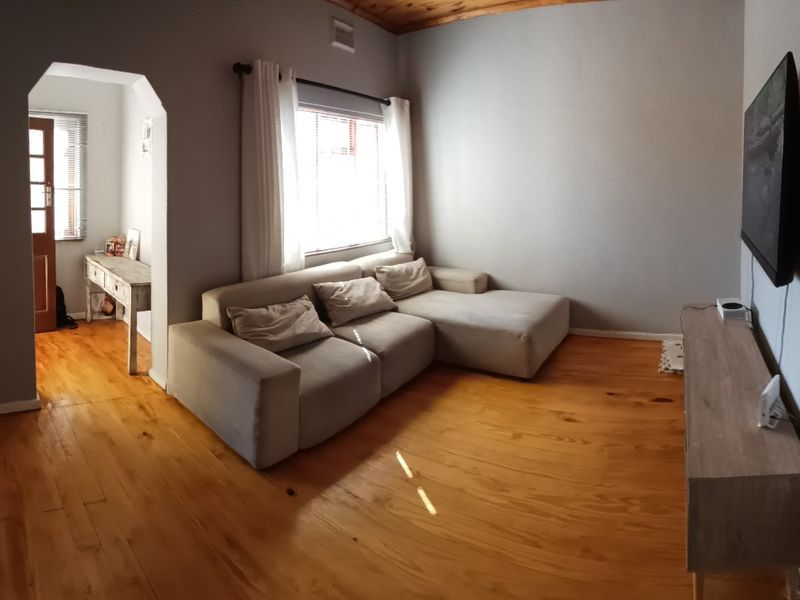A living room featuring warm timber flooring and a timber-clad ceiling, connected to an adjacent space via a character archway.