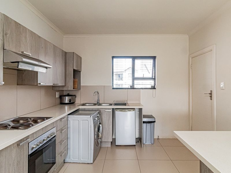 Modern kitchen featuring light wood-grain cabinetry, built-in electric oven and hob, stainless steel sink, and neutral tiled flooring with a clean, functional layout.