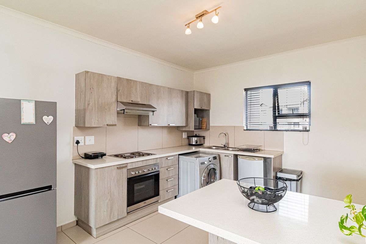 A functional kitchen featuring light wood-look cabinetry, integrated appliances, a central island, and tiled flooring, offering a clean and practical workspace.