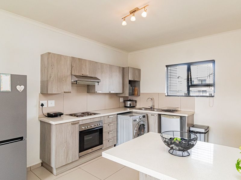 A functional kitchen featuring light wood-look cabinetry, integrated appliances, a central island, and tiled flooring, offering a clean and practical workspace.