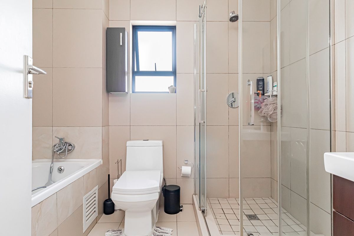 Modern bathroom featuring a glass-enclosed shower, built-in bathtub, toilet, and vanity basin with neutral wall and floor tiling.