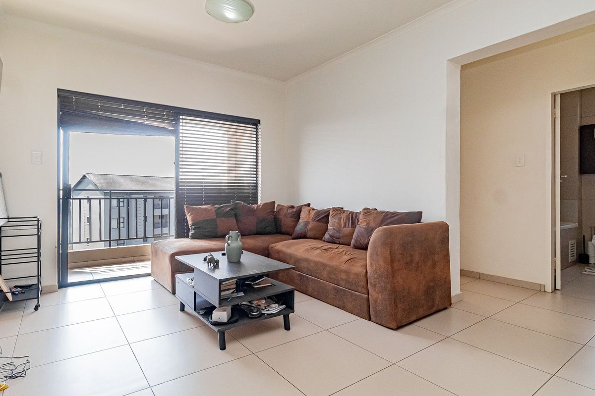 A bright living room featuring neutral tiled flooring and a sliding glass door that opens onto a balcony, providing natural light.
