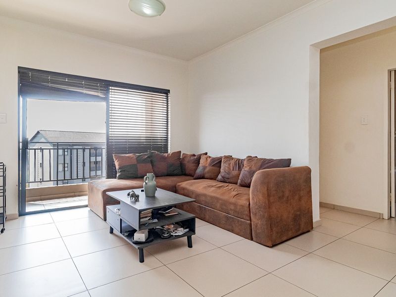 A bright living room featuring neutral tiled flooring and a sliding glass door that opens onto a balcony, providing natural light.