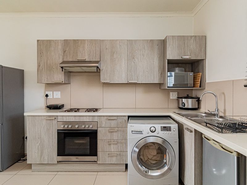 A functional kitchen featuring light wood-grain cabinetry, laminate countertops, a built-in oven with hob, and integrated laundry appliance space.