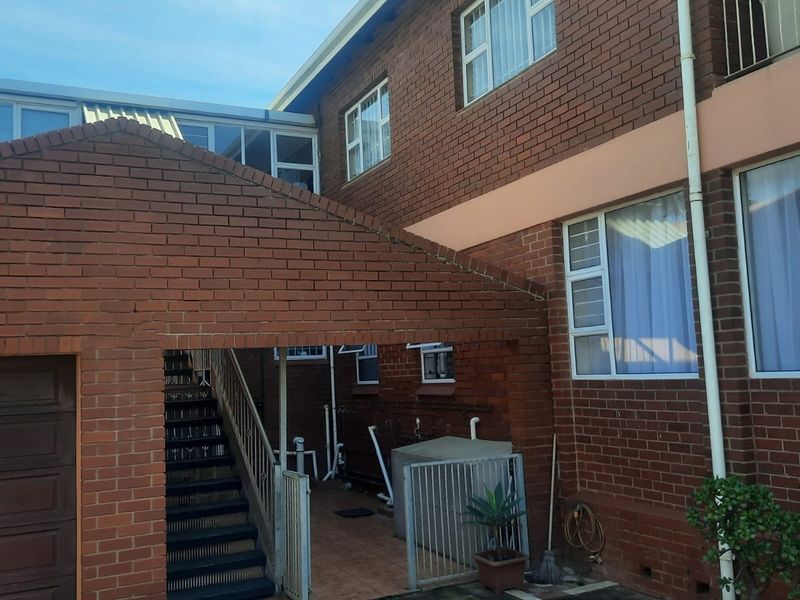 Rear exterior view of a face brick house featuring an external staircase, paved courtyard area, and aluminium window frames.