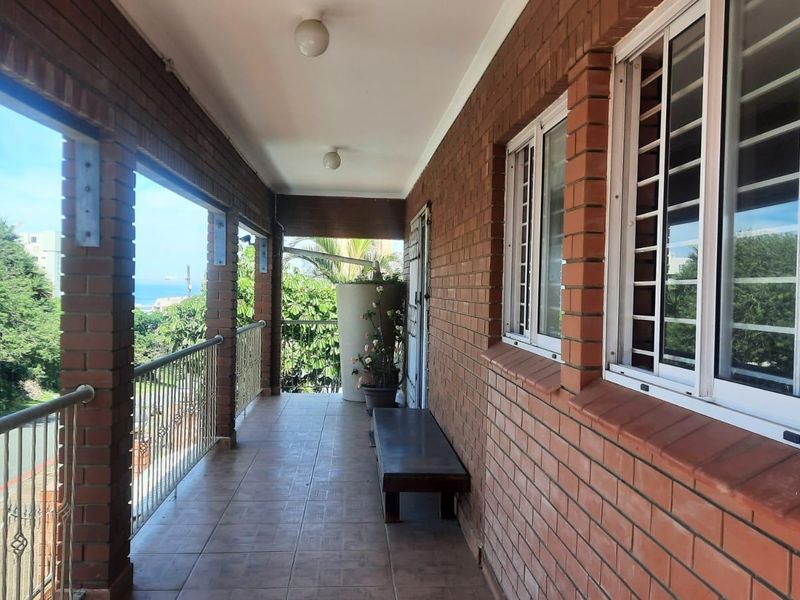 A covered balcony featuring exposed brick walls, tiled flooring, and metal security bars, offering an outdoor space with potential for seating.
