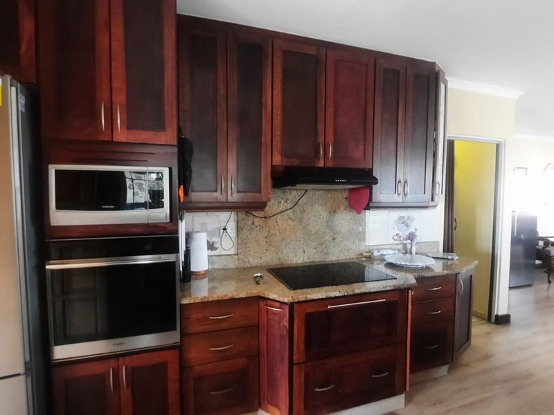 A functional kitchen featuring dark wood cabinetry, granite countertops, and integrated appliances including an oven, microwave, and electric cooktop.
