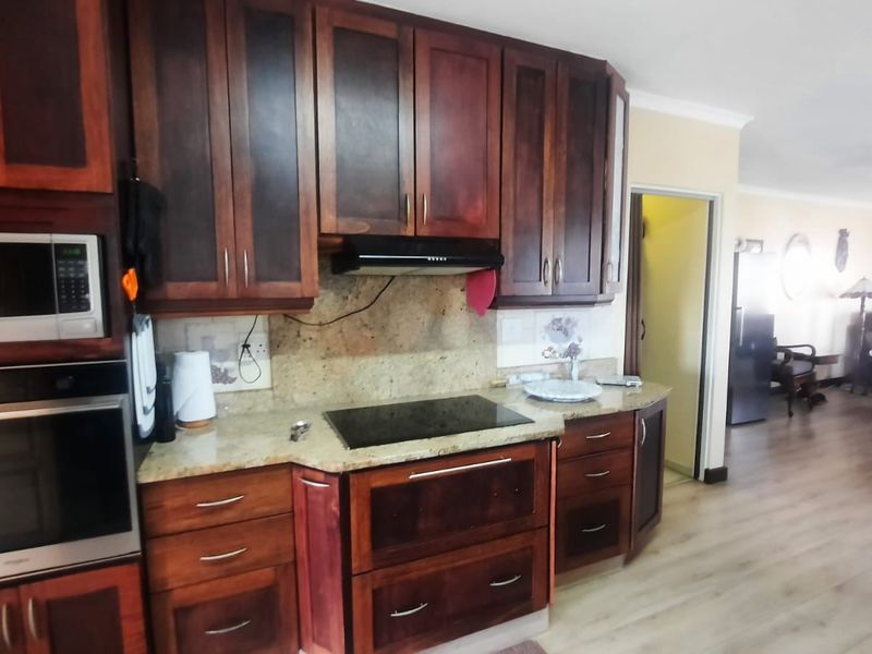 A functional kitchen featuring dark wood cabinetry, granite countertops, integrated oven, microwave, and electric hob, flowing into an open-plan living area.