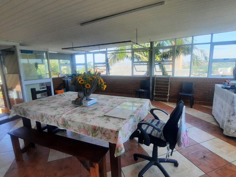 A spacious, enclosed patio area featuring tiled flooring, large windows providing natural light, and an exposed beam ceiling, suitable for versatile use.