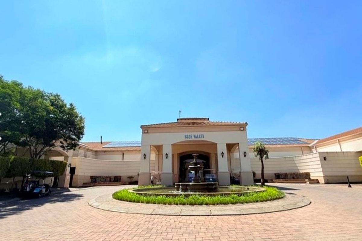 Front entrance view of the Blue Valley estate clubhouse featuring a paved driveway, central water fountain, and solar panel installation.
