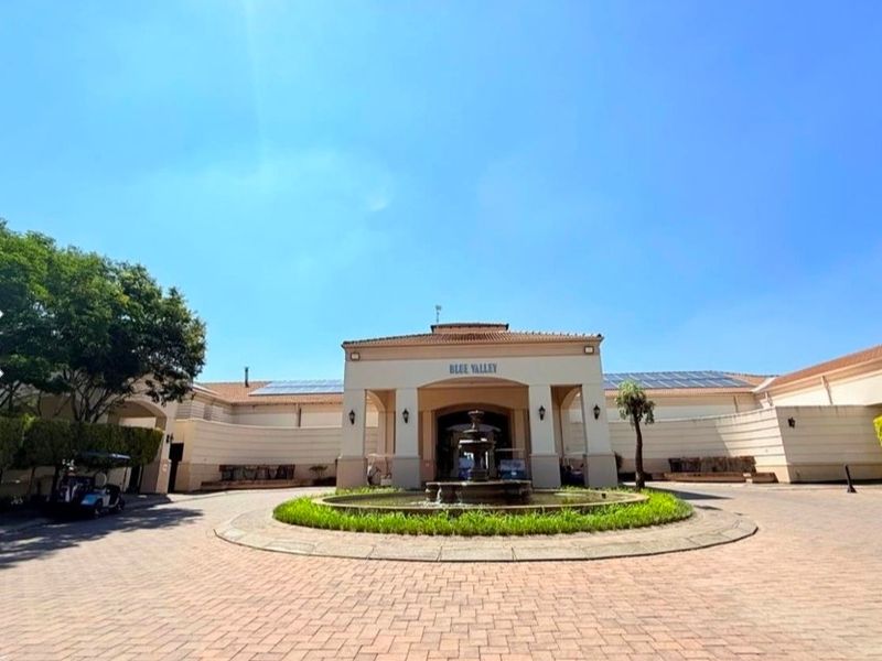 Front entrance view of the Blue Valley estate clubhouse featuring a paved driveway, central water fountain, and solar panel installation.