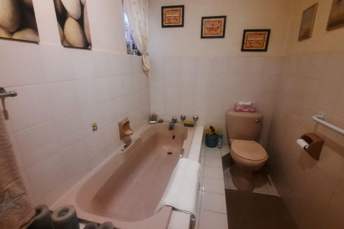 A dated bathroom featuring a built-in bathtub, toilet, and wall-to-floor tiling with a fitted grab rail.
