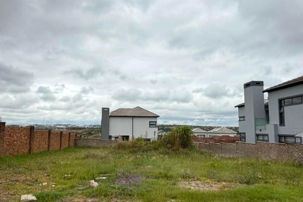 An undeveloped residential plot featuring a brick boundary wall and surrounding neighborhood views.
