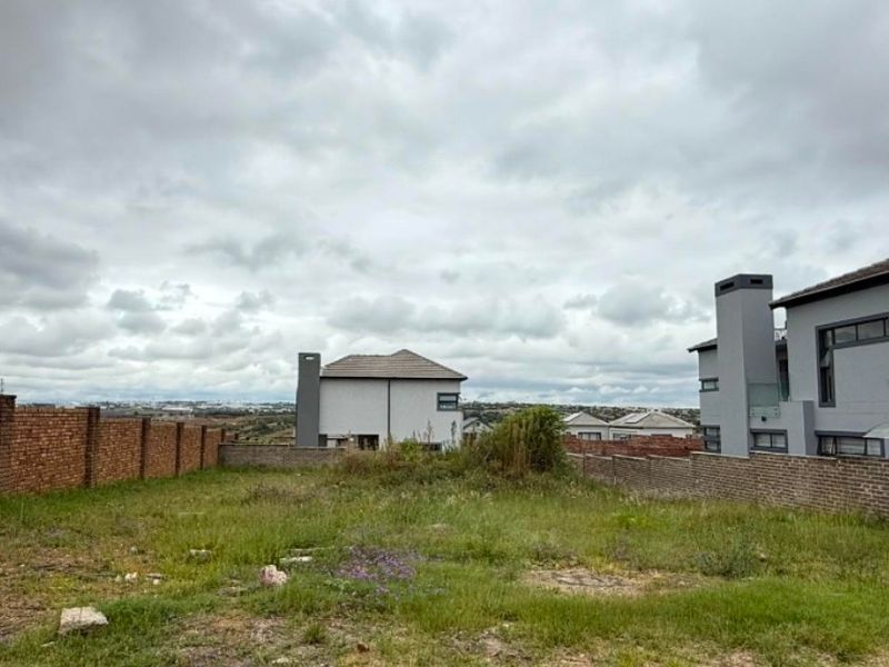 An undeveloped residential plot featuring a brick boundary wall and surrounding neighborhood views.