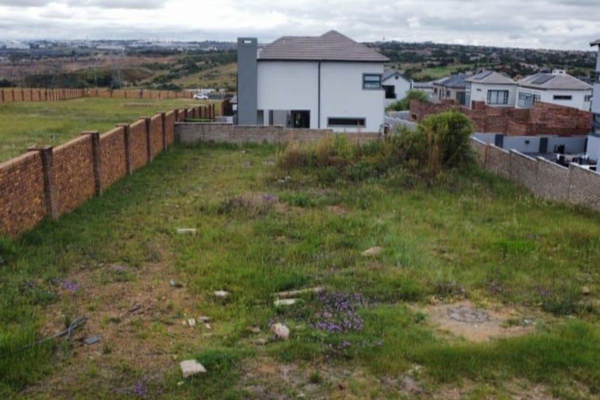 A view of a vacant residential plot enclosed by brick boundary walls, situated in a developing suburban estate.