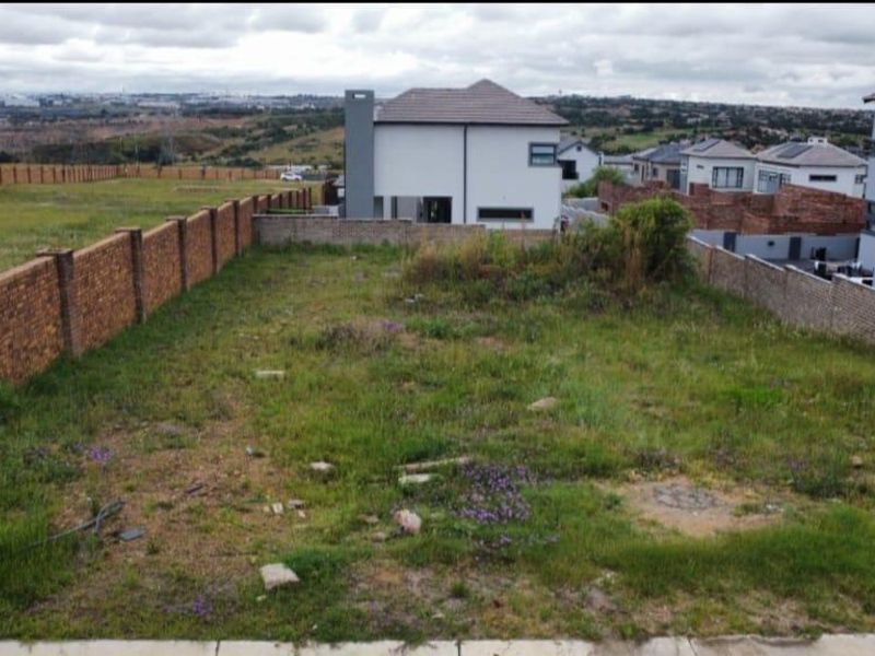 A view of a vacant residential plot enclosed by brick boundary walls, situated in a developing suburban estate.
