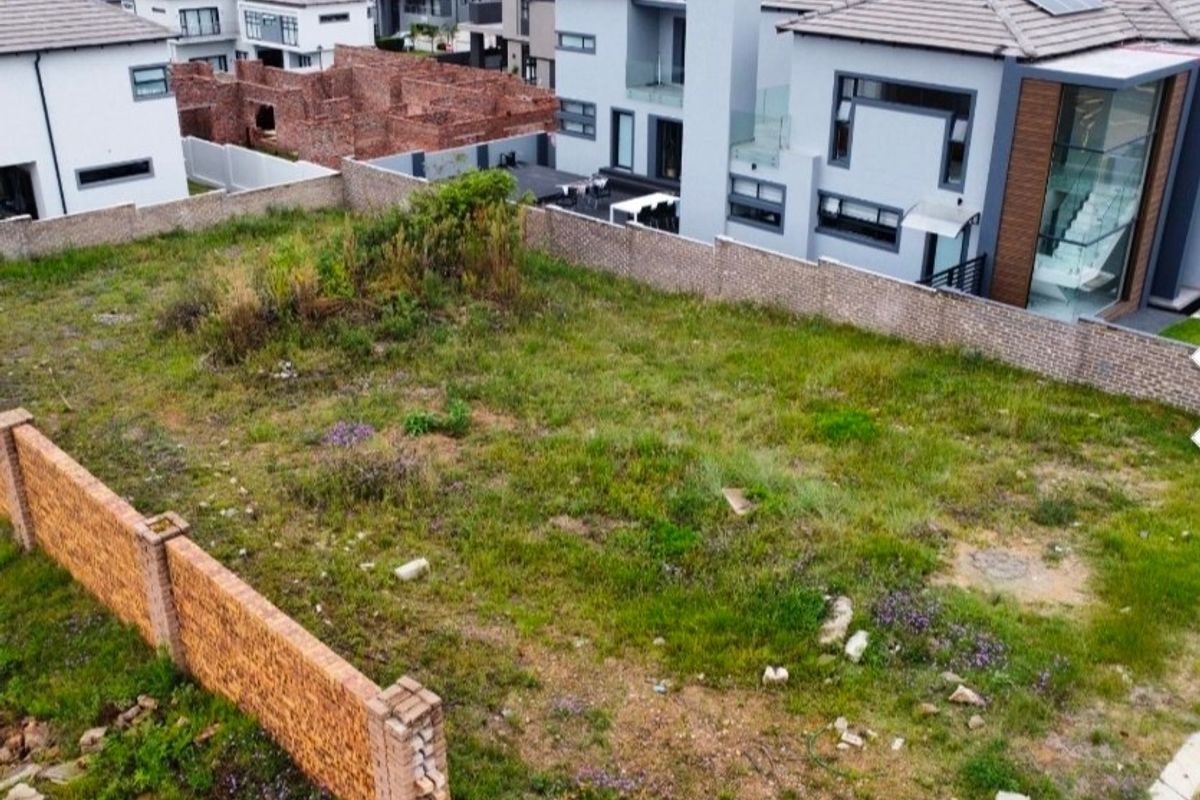 An aerial view of a vacant residential plot enclosed by brick boundary walls, situated within a modern suburban estate.