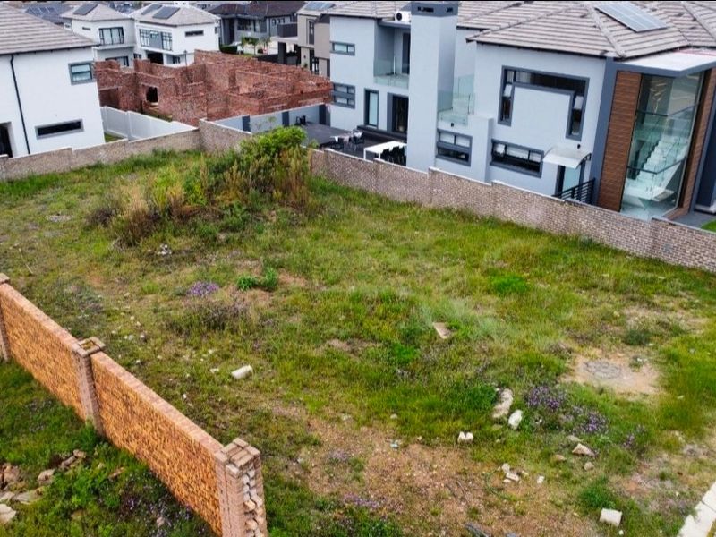 An aerial view of a vacant residential plot enclosed by brick boundary walls, situated within a modern suburban estate.