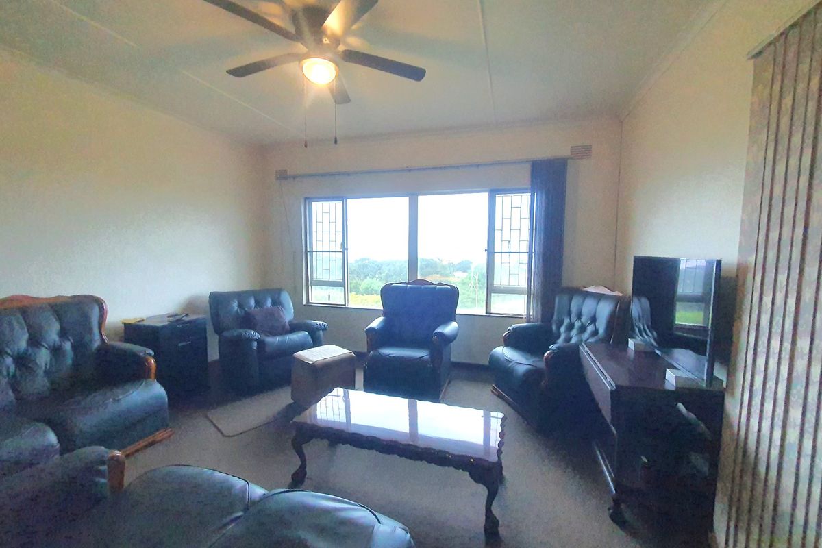 A living room featuring a ceiling fan, large windows with security bars, and vertical blinds, offering a functional space with natural light.
