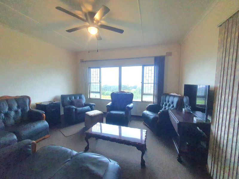 A living room featuring a ceiling fan, large windows with security bars, and vertical blinds, offering a functional space with natural light.
