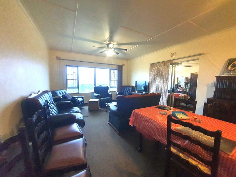 Spacious open-plan living and dining area featuring a ceiling fan, large windows with security bars, and direct access to an adjacent room.