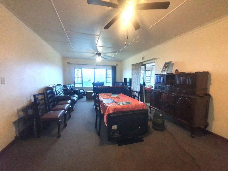 Spacious living area featuring a ceiling fan, large windows, and sliding door access, offering a blank canvas for modernization and updated flooring.
