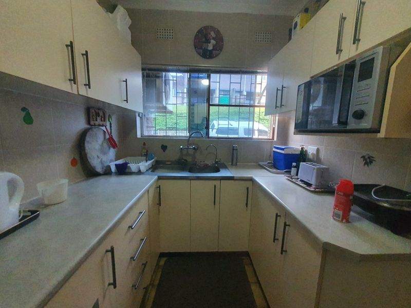 A functional galley-style kitchen featuring built-in cabinetry, laminate countertops, a stainless steel double sink, and a built-in microwave.